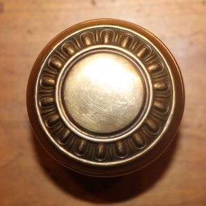 May include: A round, brass door knob with a decorative, ornate design around the edge.