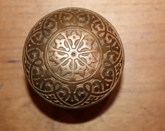 May include: A round, ornate brass door knob with a detailed floral design.