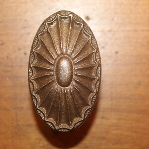 May include: A vintage oval-shaped brass door knob with a sunburst design.