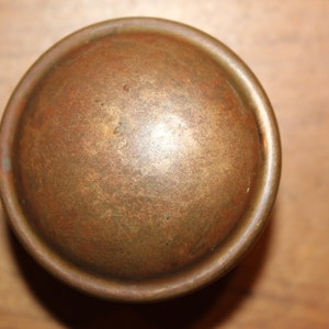 May include: A round, brass door knob with a slightly raised, smooth surface. The knob has a worn, aged patina.