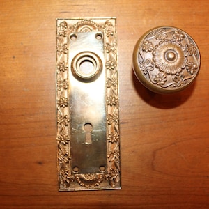 May include: A set of antique brass door hardware with a floral design. The set includes a door knob and a backplate.