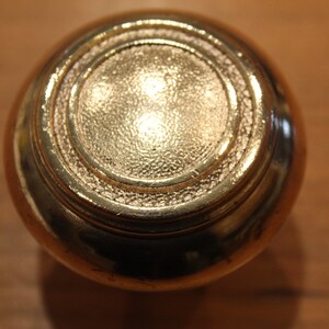 May include: A round, gold-colored door knob with a raised, textured center and a decorative ring around the edge.