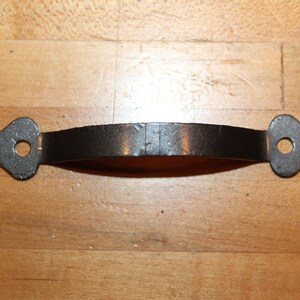 May include: Black metal door handle with a curved shape and pointed ends. The handle has two holes for mounting.