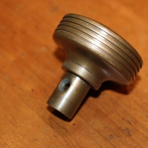 May include: A brass level with a round, grooved top and a threaded shaft. The level is designed for use in woodworking or other crafts.