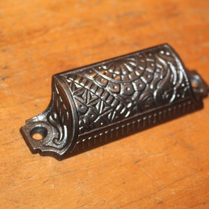 May include: Black cast iron drawer pull with an ornate design. The pull has a curved shape and a decorative pattern on the top.
