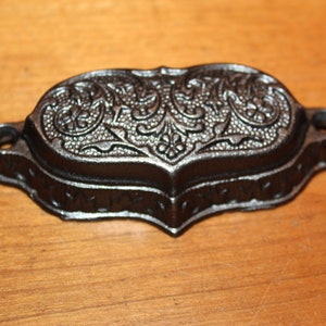 May include: A black cast iron drawer pull with an ornate floral design.