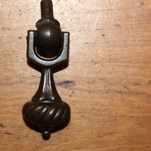 May include: A black metal cabinet knob with a round, ornate design. The knob has a decorative, twisted base.