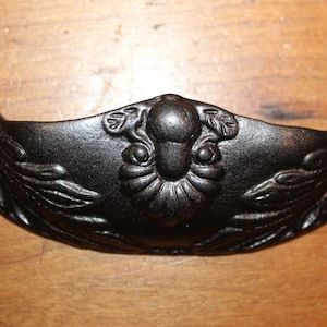 May include: Black cast iron drawer pull with a floral design. The pull has a rounded shape and two holes for mounting.