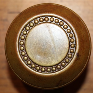May include: A round, brass door knob with a decorative border of small, raised dots.
