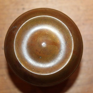 May include: A round, brass door knob with a raised, circular design in the center.