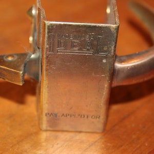 May include: A vintage brass door handle with a square backplate. The backplate has the text "Made in USA IDEAL PAT. APPL'D FOR" engraved on it.