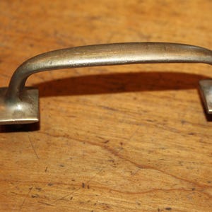 May include: A silver-toned metal cabinet door pull with a rounded top and square ends.