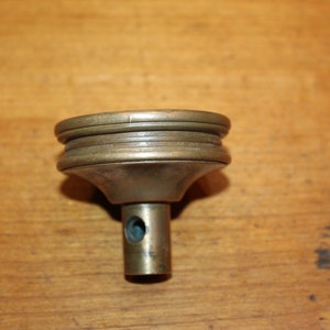 May include: A brass level with a round base and a threaded stem. The level has a small hole in the center of the base.
