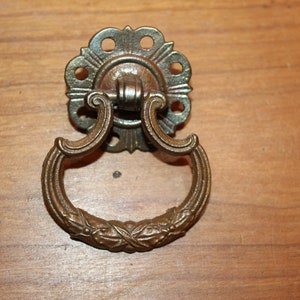May include: A vintage, ornate, brass drawer pull with a ring handle and a decorative floral design.