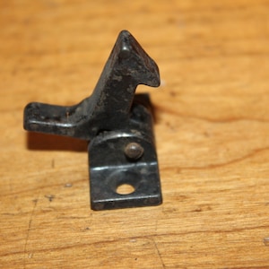 May include: Black metal latch with a hook and a square base. The latch is designed to be used on a door or cabinet.