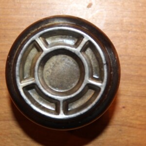 May include: A black and silver round door knob with a decorative design. The knob has a circular center with a ring of six evenly spaced, rounded, raised sections.