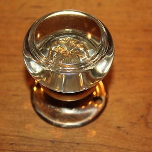 May include: A clear glass door knob with a decorative pattern on the top and a brass base.