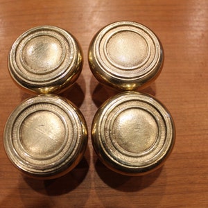 May include: Four gold-toned door knobs with a circular design. Each knob has a raised center circle surrounded by two concentric rings.