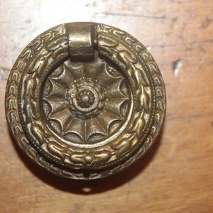 May include: A brass door pull with a decorative floral design around the edge. The pull has a ring shape and a detailed center design.
