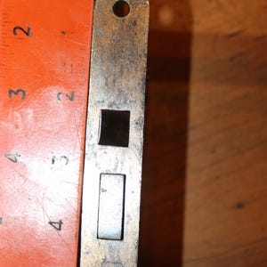 May include: A brass door lock plate with two keyholes and a round hole at the top and bottom. The plate is about 4 inches tall.
