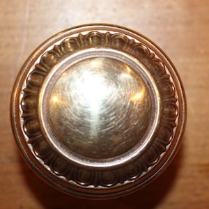 May include: A round, brass door knob with a decorative, scalloped edge. The knob has a shiny, polished finish.