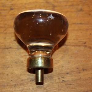 May include: A clear glass door knob with a brass base and a metal screw. The knob is round and has a slight teardrop shape.