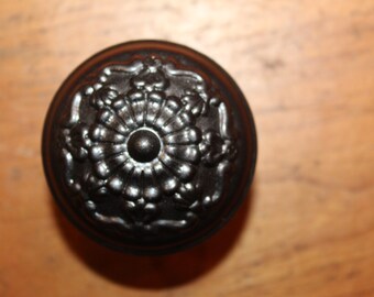 May include: A black metal knob with a decorative floral design.