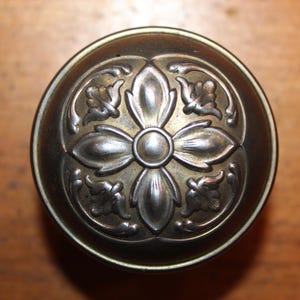 May include: A round, silver-toned door knob with a decorative floral design.