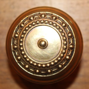 May include: A round, brass door knob with a decorative, beaded border.