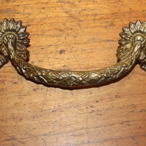 May include: A decorative brass drawer pull with a floral design. The pull is shaped like a half-circle with a curved handle.