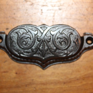 May include: A black cast iron drawer pull with a decorative floral design.