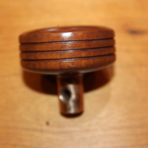 Puede incluir: Un pomo de madera con un poste de metal roscado. El pomo tiene un acabado marrón oscuro y cuatro anillos en relieve.