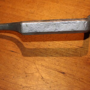 May include: A cast iron spur with a floral design on the heel plate and a decorative end. The spur is silver in color and has a rectangular shank. The spur is designed to be attached to a riding boot.