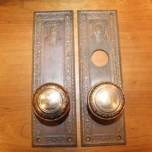 May include: A pair of antique brass door plates with ornate designs and matching round door knobs.