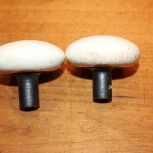 May include: Two white ceramic mushroom-shaped door knobs with black metal stems.