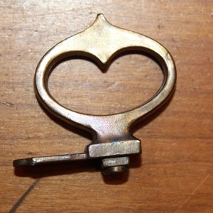 May include: A brass key with a heart-shaped handle and a small, flat key bit. The key is worn and has a patina.