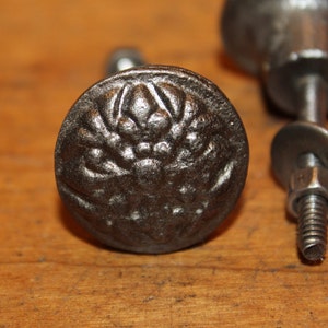 May include: A black metal cabinet knob with a floral design. The knob has a screw on the back for attaching to a cabinet door.