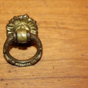 May include: A brass drawer pull with a decorative floral design and a ring-shaped handle.