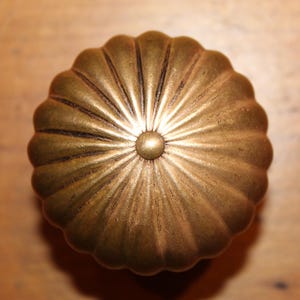 May include: A decorative, antique-style cabinet knob with a fluted, pumpkin-shaped design. The knob is made of brass with a golden finish and a small, round center. The knob is likely used for furniture or cabinetry.