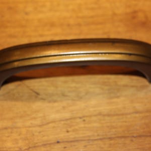 May include: A bronze-toned cabinet pull handle with a curved design. The handle has a dark brown base with a gold-colored top section. The handle is approximately 6 inches long.