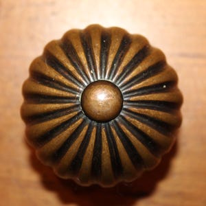 May include: A round, brass door knob with a fluted design. The knob has a dark brown finish and a raised center.