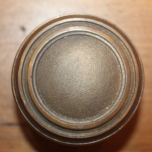 May include: A round, brass door knob with a concentric circle design. The knob has a smooth, slightly textured surface.