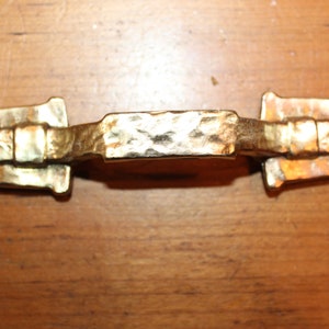 May include: A gold-toned metal cabinet pull with a hammered finish. The pull has a rectangular shape with rounded edges and a raised center section.