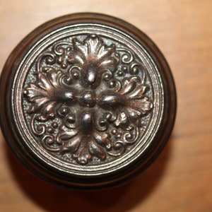 May include: A round, ornate, metal door knob with a detailed floral design. The knob is a dark bronze color.