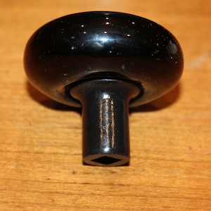 May include: Black ceramic door knob with a square-shaped keyhole. The knob has a shiny finish and a raised, rounded top.