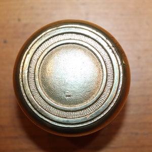 May include: A round, brass door knob with a concentric circle design.