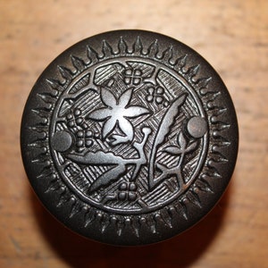 May include: A black metal door knob with a floral design. The knob has a circular shape with a raised rim and a decorative pattern of leaves and flowers.