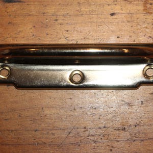 May include: A gold-toned metal door handle with a rounded top and three screw holes.