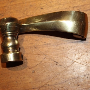 May include: A vintage brass furniture handle with a curved, ergonomic design. The handle features a rounded base and a smooth, polished surface. The brass has a warm, golden hue, suggesting age and use. The handle is likely for a drawer or cabinet.