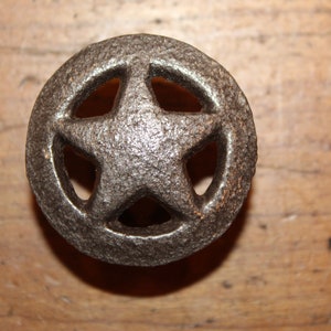 May include: A round, silver-toned metal knob with a five-pointed star cut-out design. The star has a textured surface.